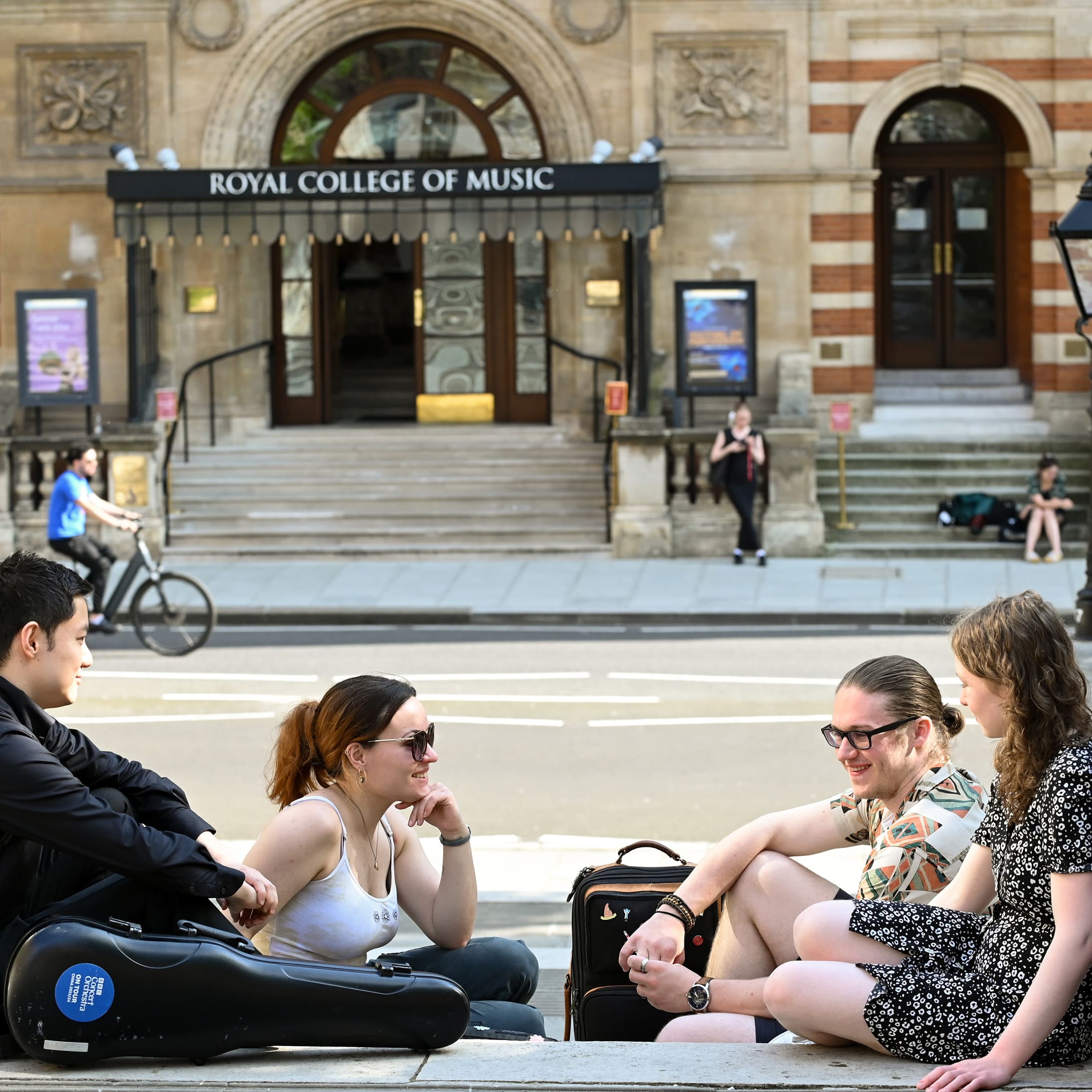 A group of students walking away from the front of the college on a sunny day.